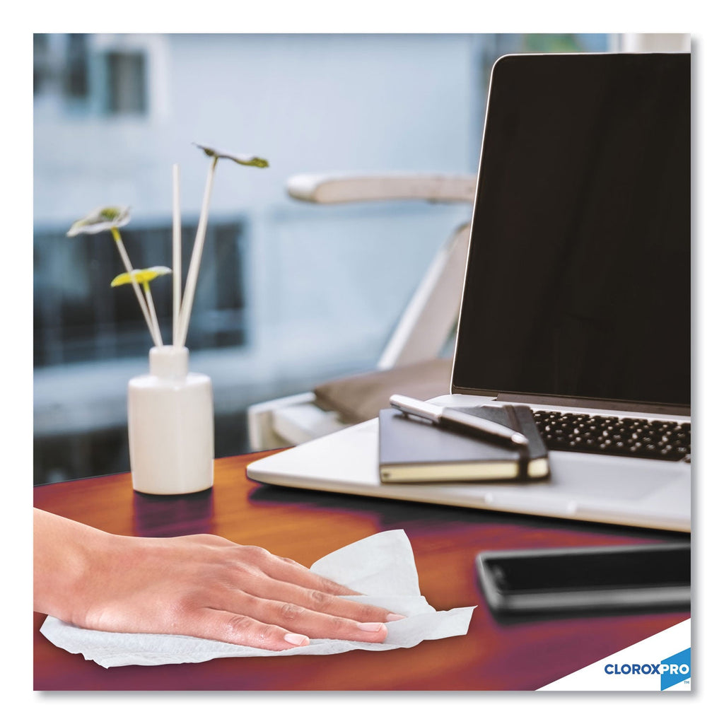 Person cleaning a desk with Clorox wipes, laptop, phone, and books in the background.