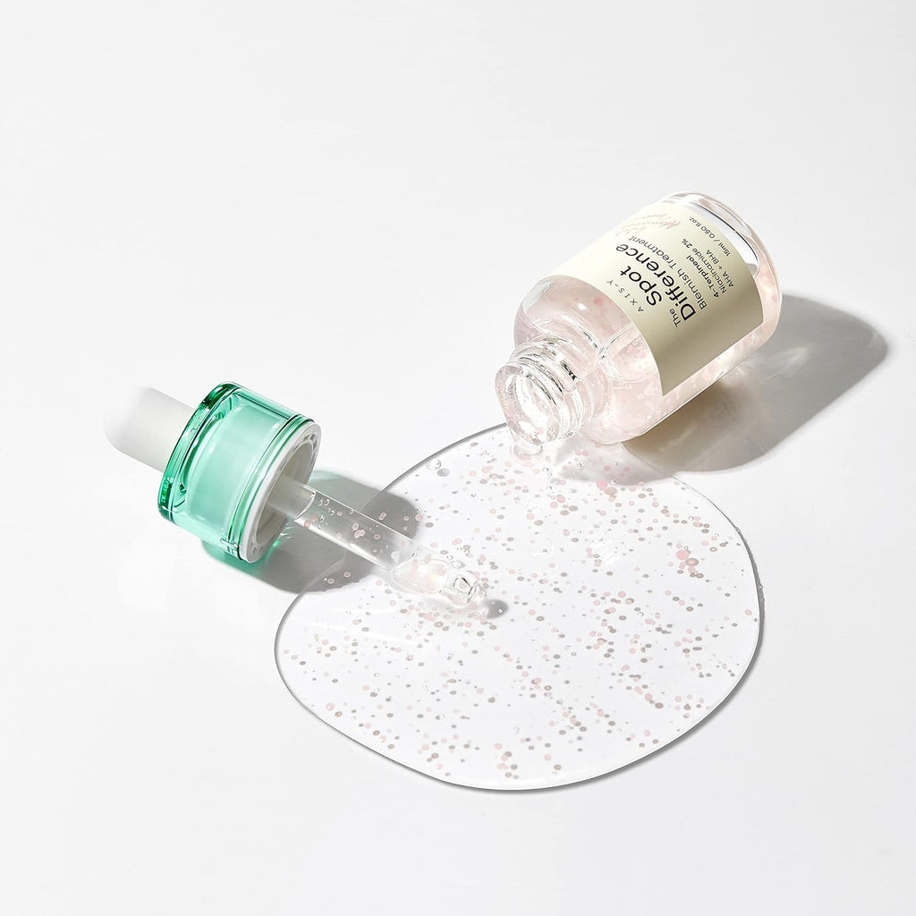 AXIS-Y Spot The Difference Blemish Treatment bottle with detached green dropper beside a clear serum spill containing pink ceramide capsules on a clean white background.