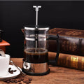 French press coffee maker with heat-resistant glass carafe, stainless steel plunger and filter, black handle, brewed coffee, coffee beans and vintage books on wooden table