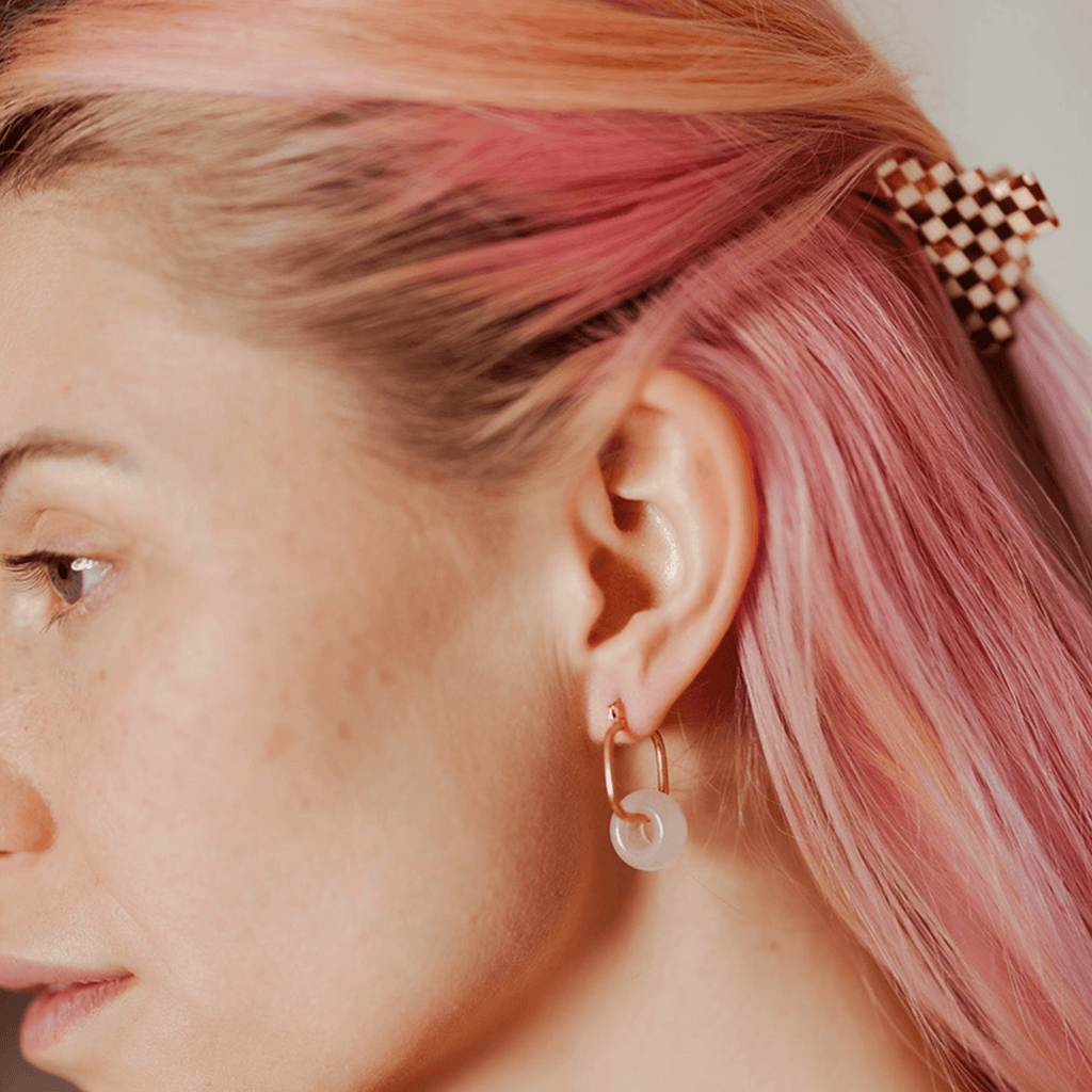 Pink hair with red and white checkered small pyramid hair claw clip and gold hoop earring with translucent white charm, trendy women's hair accessory.