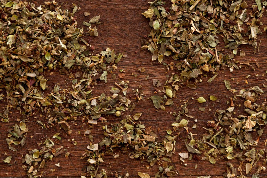 Dried gourmet herb and spice blend scattered across a rustic wooden surface, showcasing fresh, aromatic seasoning for cooking and culinary creations.