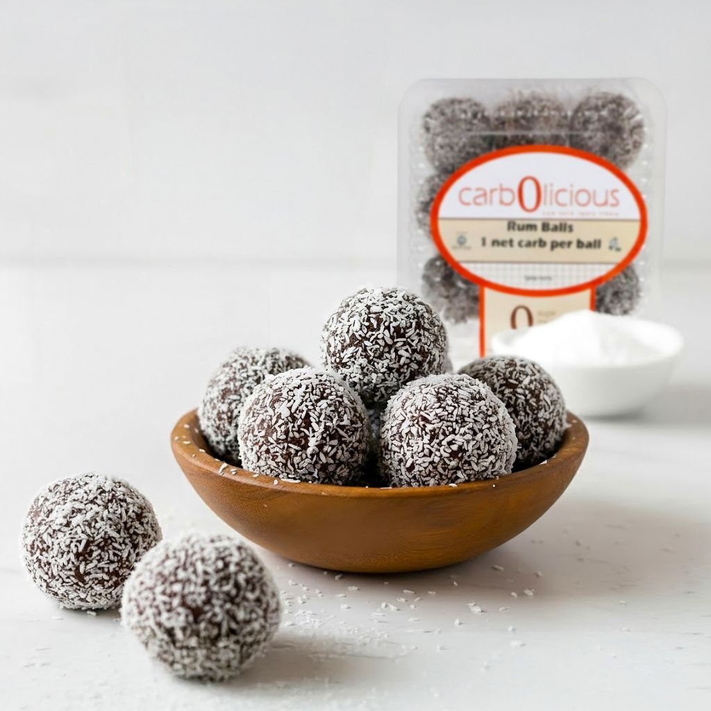 Carbolicious sugar-free rum balls coated in coconut flakes, displayed in a wooden bowl with branded low-carb keto-friendly packaging in the background.