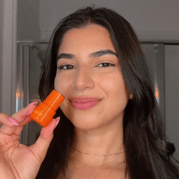 Woman applying AMINNAH Fruit Loops LOLLIPOP Lips & Cheeks Tint in Coral, clean beauty lip and cheek stain with natural ingredients, cruelty-free, vegan, paraben-free, gluten-free makeup in recyclable packaging from a female-owned brand for a fresh radiant glow.