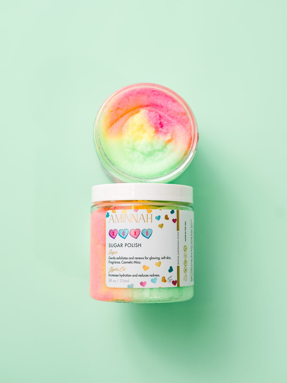XOXO Sugar Scrub by Aminnah open jar with colorful pastel sugar polish, vegan clean beauty body scrub made with natural ingredients, cruelty-free skincare, female-owned brand, moisturizing exfoliating scrub for soft, smooth, glowing skin