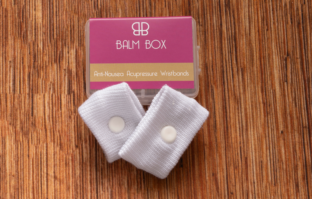 White Anti-Nausea Acupressure Wristbands by The Balm Box in Pink Packaging, Natural Drug-Free Motion Sickness and Nausea Relief Wristbands for Wellness, Travel, Pregnancy, Chemotherapy Care and Self-Care Gifts, Shown on a Wooden Surface