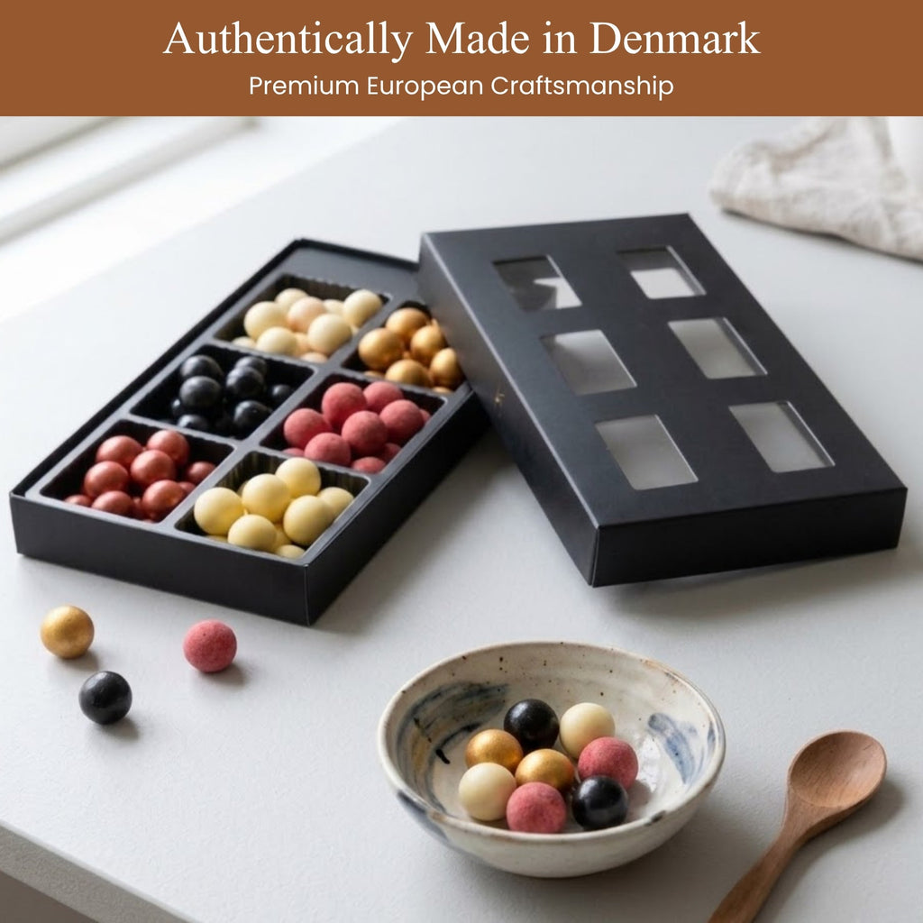 Black decorative box with colorful spherical items, a bowl with similar items, and a wooden spoon on a white surface. Text 'Authentically Made in Denmark' and 'Premium European Craftsmanship' at the top.