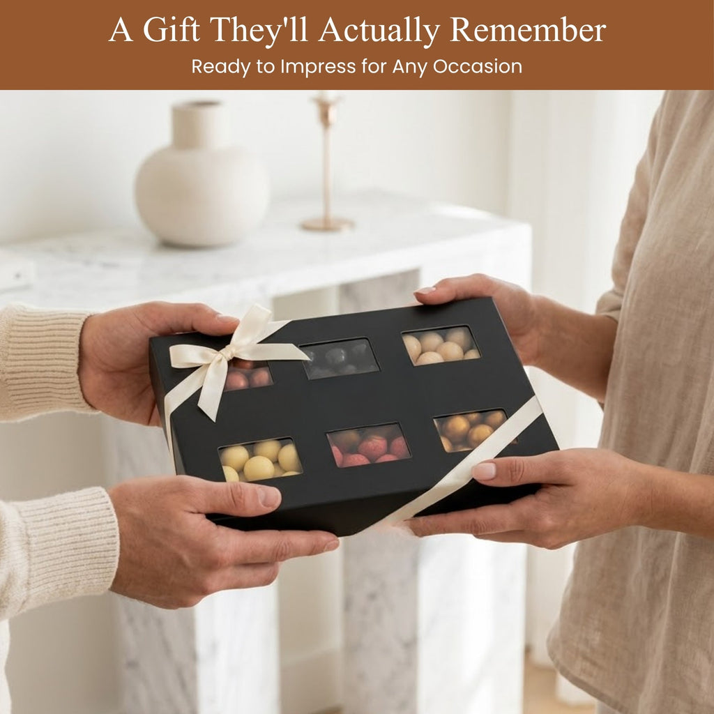 Two people exchanging a black gift box with chocolates, set against a blurred indoor background.