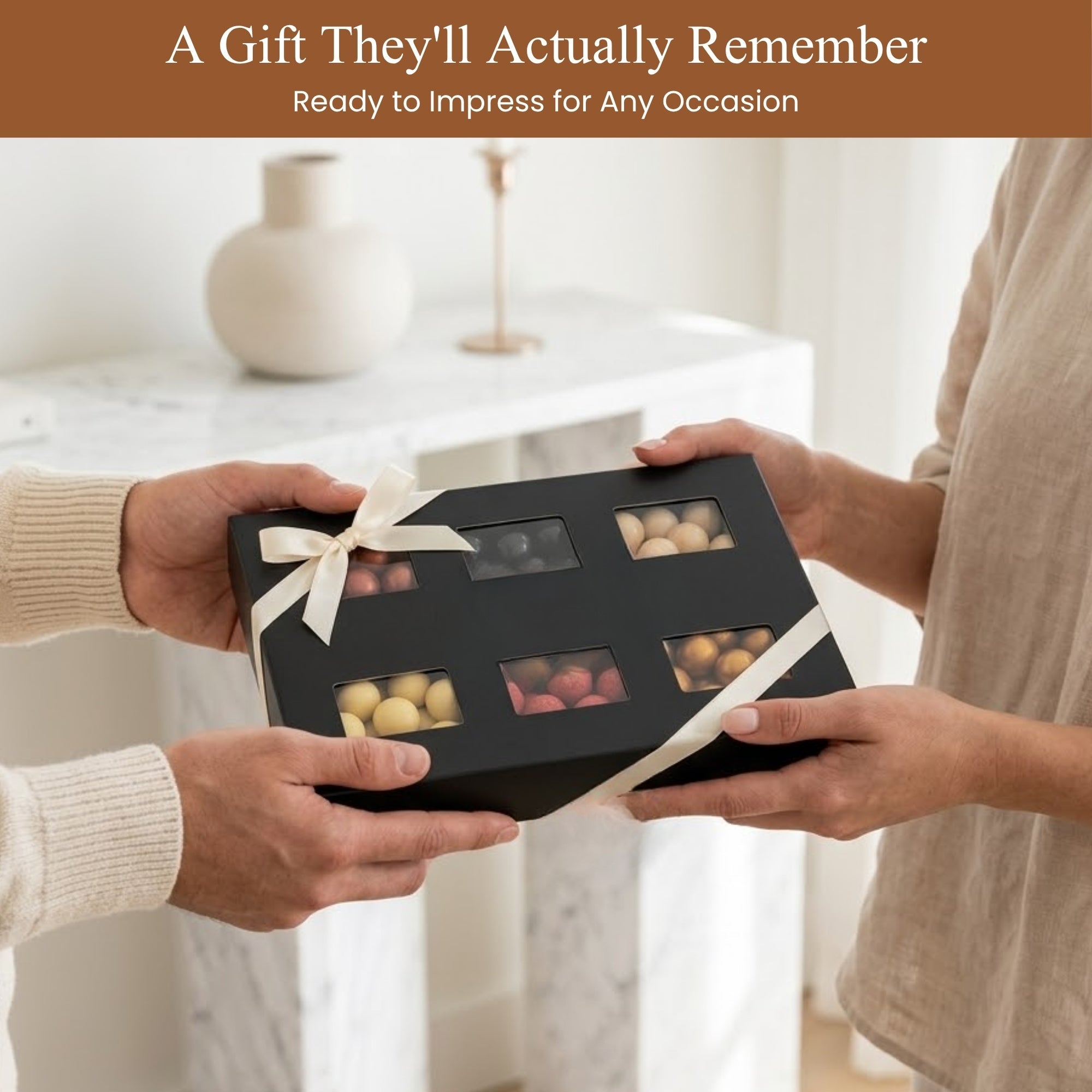 Two people exchanging a black gift box with chocolates, set against a blurred indoor background.