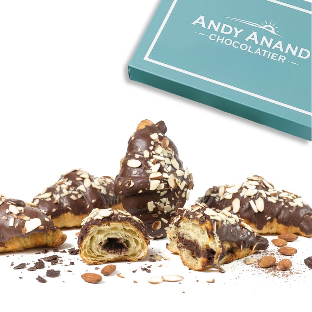 Chocolate-dipped pastries with nuts on a white surface, Andy Anand Chocolatier box in the background.