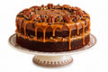 Chocolate cake with caramel sauce and pecans on a decorative cake stand.