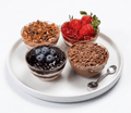 Four dessert bowls with different toppings on a white plate with a spoon.