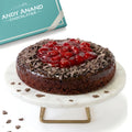 Chocolate cake with cherry topping on a marble stand, Andy Anand Chocolatier box in the background.