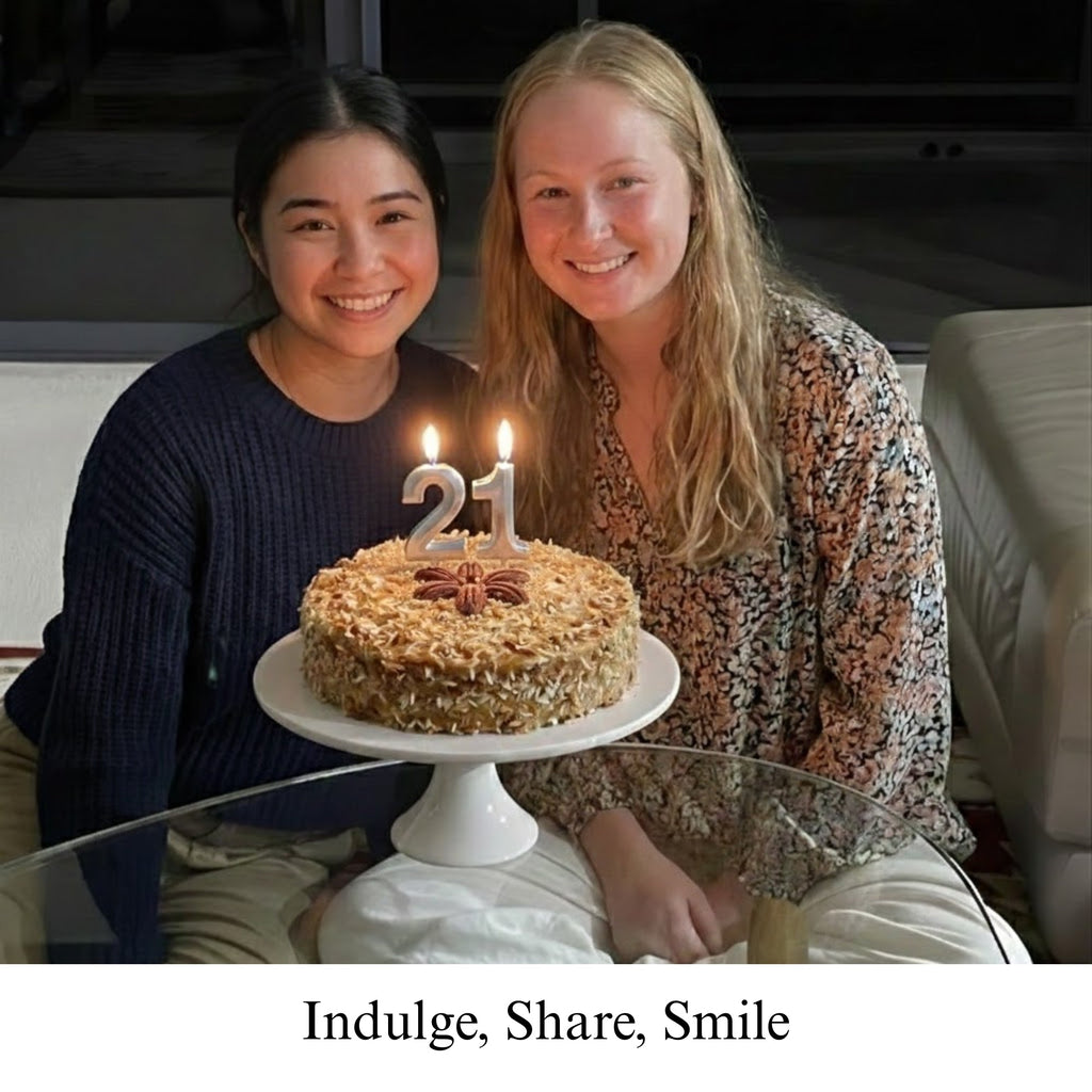 Two women sitting with a birthday cake featuring the number 21 candles, with text 'Indulge, Share, Smile' at the bottom.