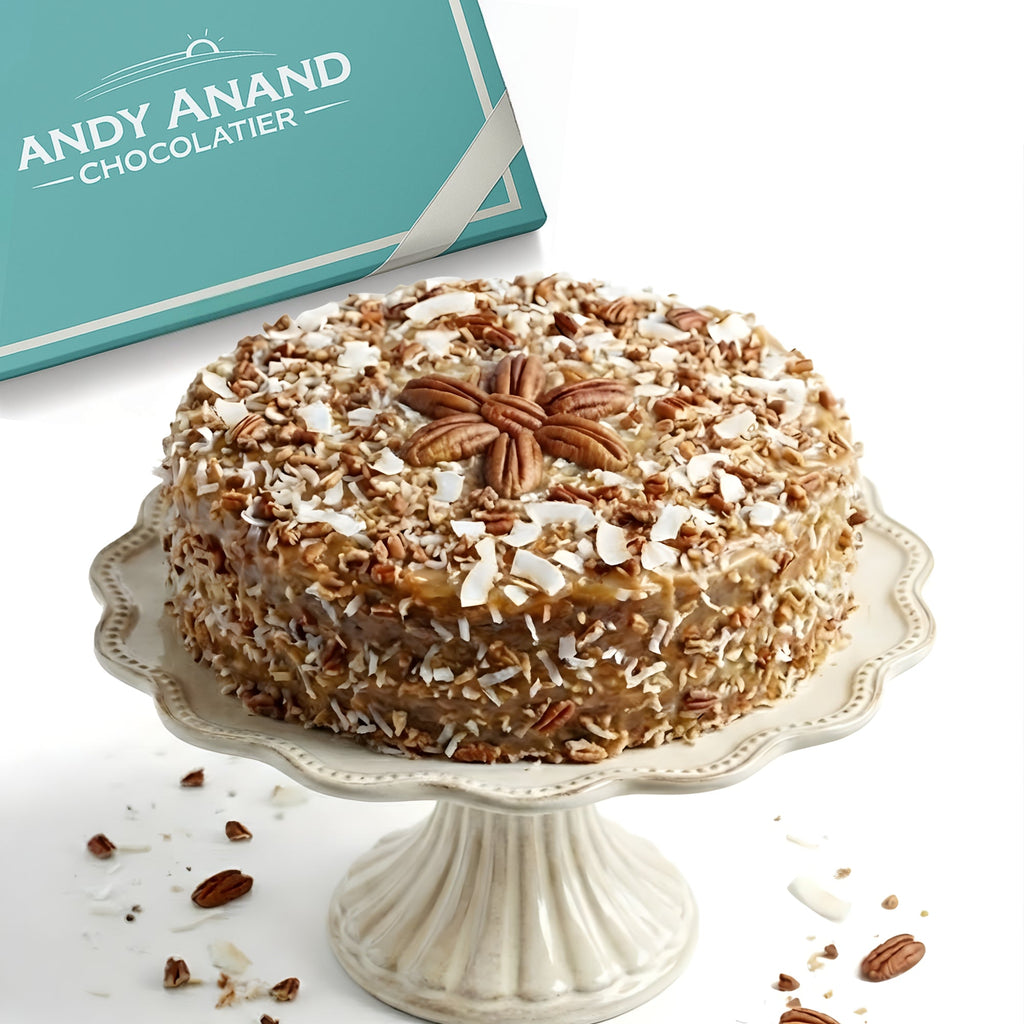 Decorative cake with pecans on a white stand next to an Andy Anand Chocolatier box.
