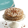 Decorative cake with pecans on a white stand next to an Andy Anand Chocolatier box.