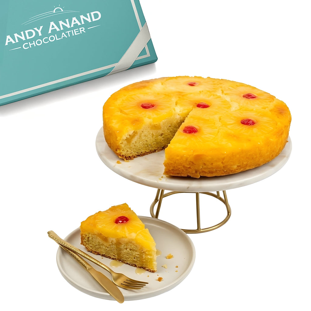 Pineapple upside-down cake with a slice on a plate, next to a box labeled 'Andy Anand Chocolatier'.