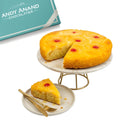 Pineapple upside-down cake with a slice on a plate, next to a box labeled 'Andy Anand Chocolatier'.