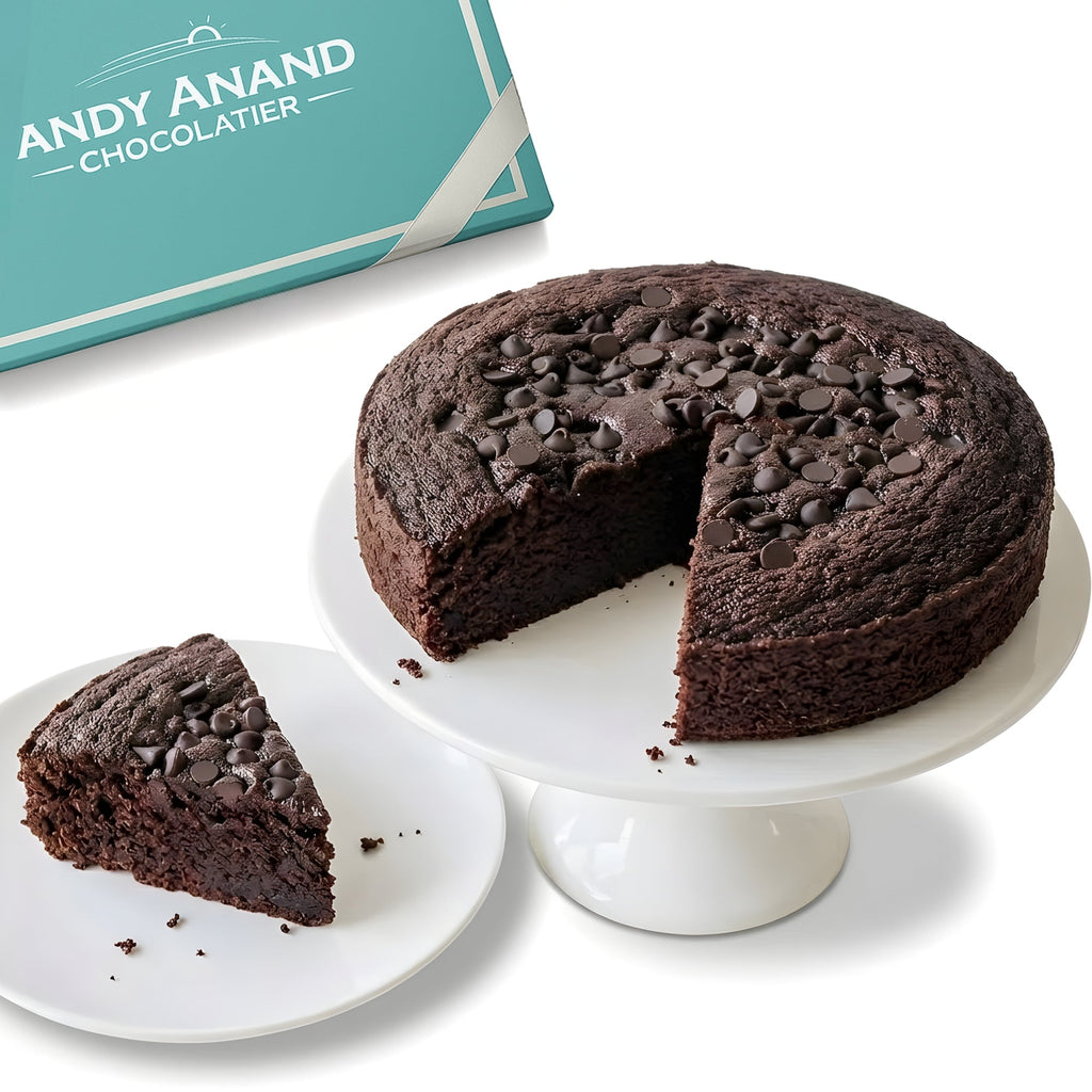 Chocolate cake with a slice taken out on a white stand, next to a 'Andy Anand Chocolatier' box.