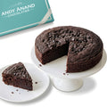 Chocolate cake with a slice taken out on a white stand, next to a 'Andy Anand Chocolatier' box.
