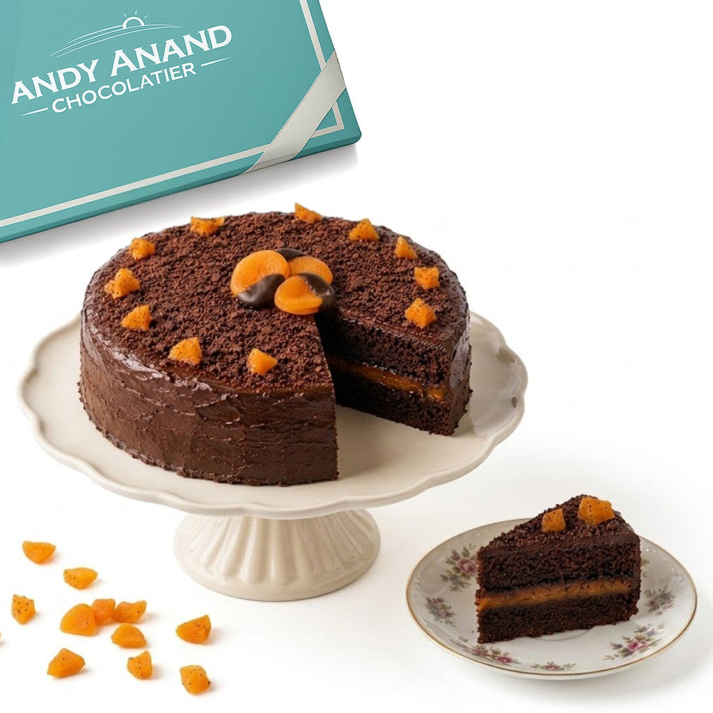 Chocolate cake with a slice taken out, displayed on a cake stand with 'Andy Anand Chocolatier' branding.