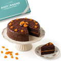 Chocolate cake with a slice taken out, displayed on a cake stand with 'Andy Anand Chocolatier' branding.