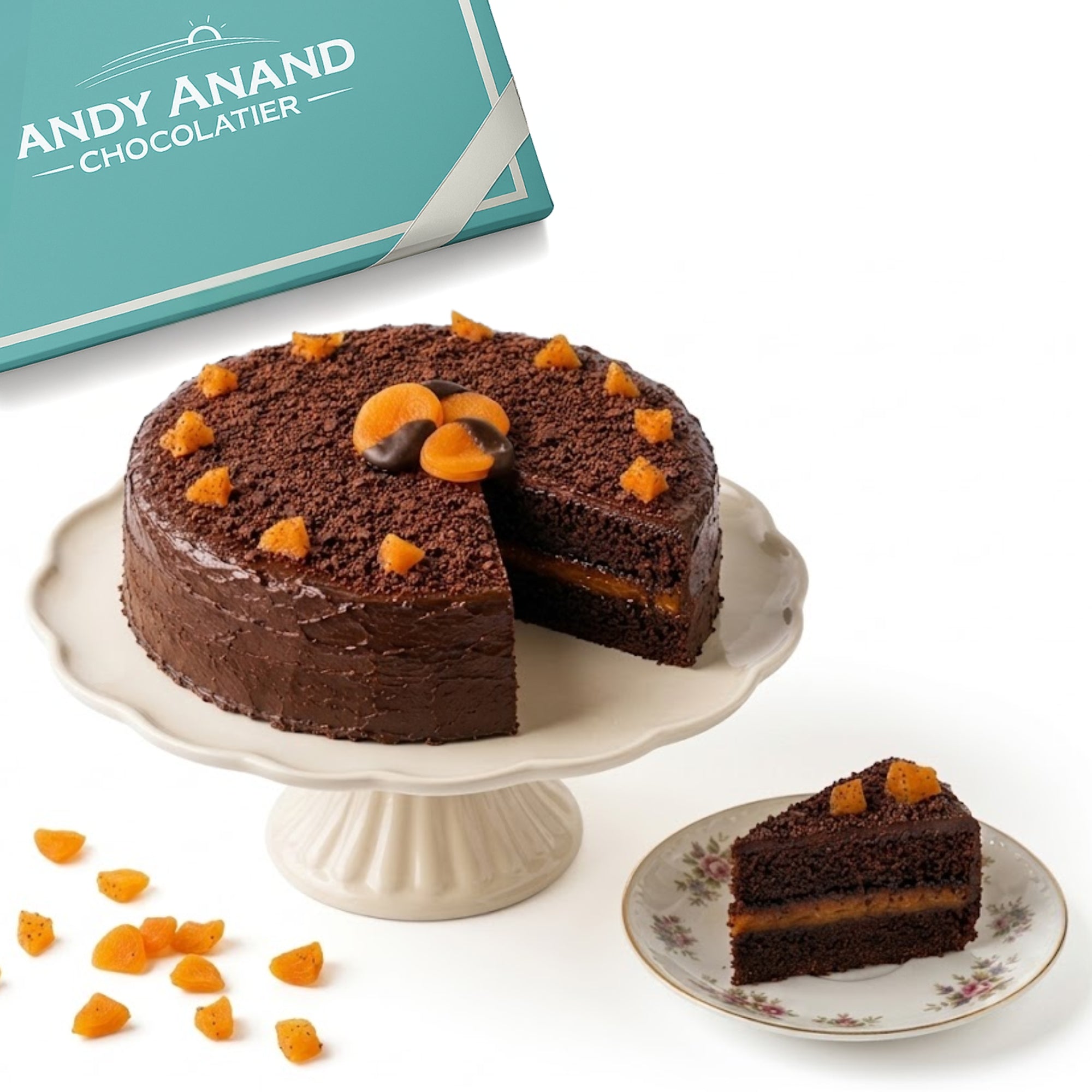 Chocolate cake with a slice taken out, displayed on a cake stand with 'Andy Anand Chocolatier' branding.