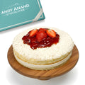 Cheesecake with strawberries and red sauce on a wooden board, branded by Andy Anand Chocolatier.