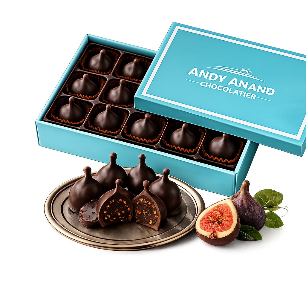 Chocolate-covered figs in a turquoise box with 'Andy Anand Chocolatier' branding, surrounded by fresh figs on a white background.