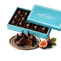 Chocolate-covered figs in a turquoise box with 'Andy Anand Chocolatier' branding, surrounded by fresh figs on a white background.