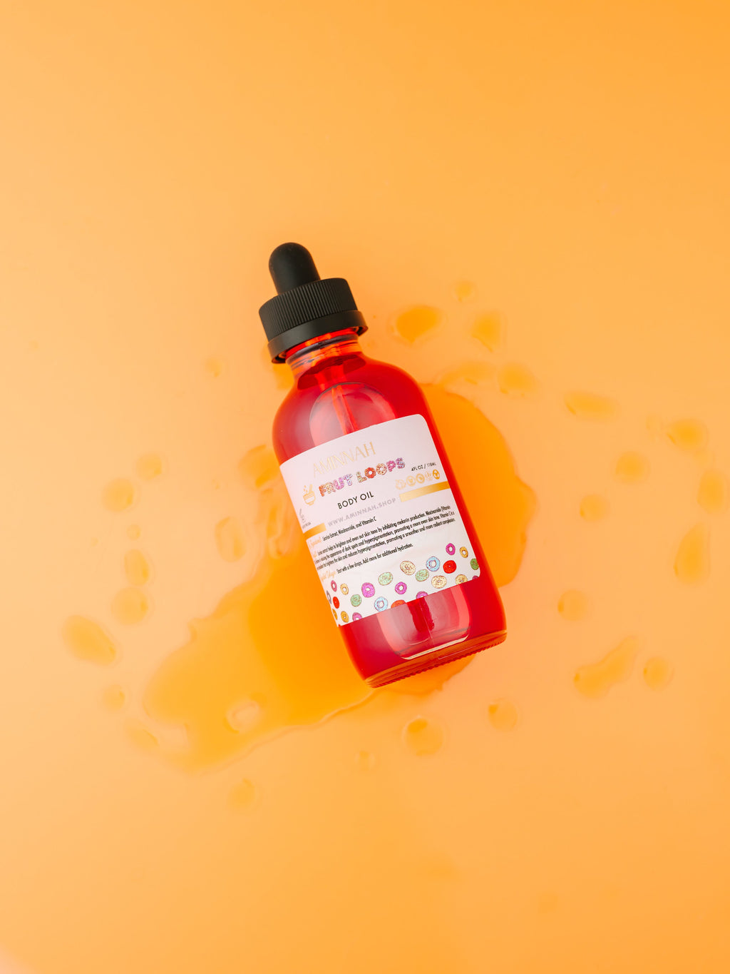 Frut Loops Body Oil in a vibrant red dropper bottle on a soft yellow background with nourishing body oil droplets. Clean beauty, cruelty-free, vegan skincare made with natural ingredients including niacinamide, licorice extract, and vitamin C to hydrate, brighten, and promote glowing skin. Premium body oil from a female-owned brand with a sweet fruity cereal-inspired scent.