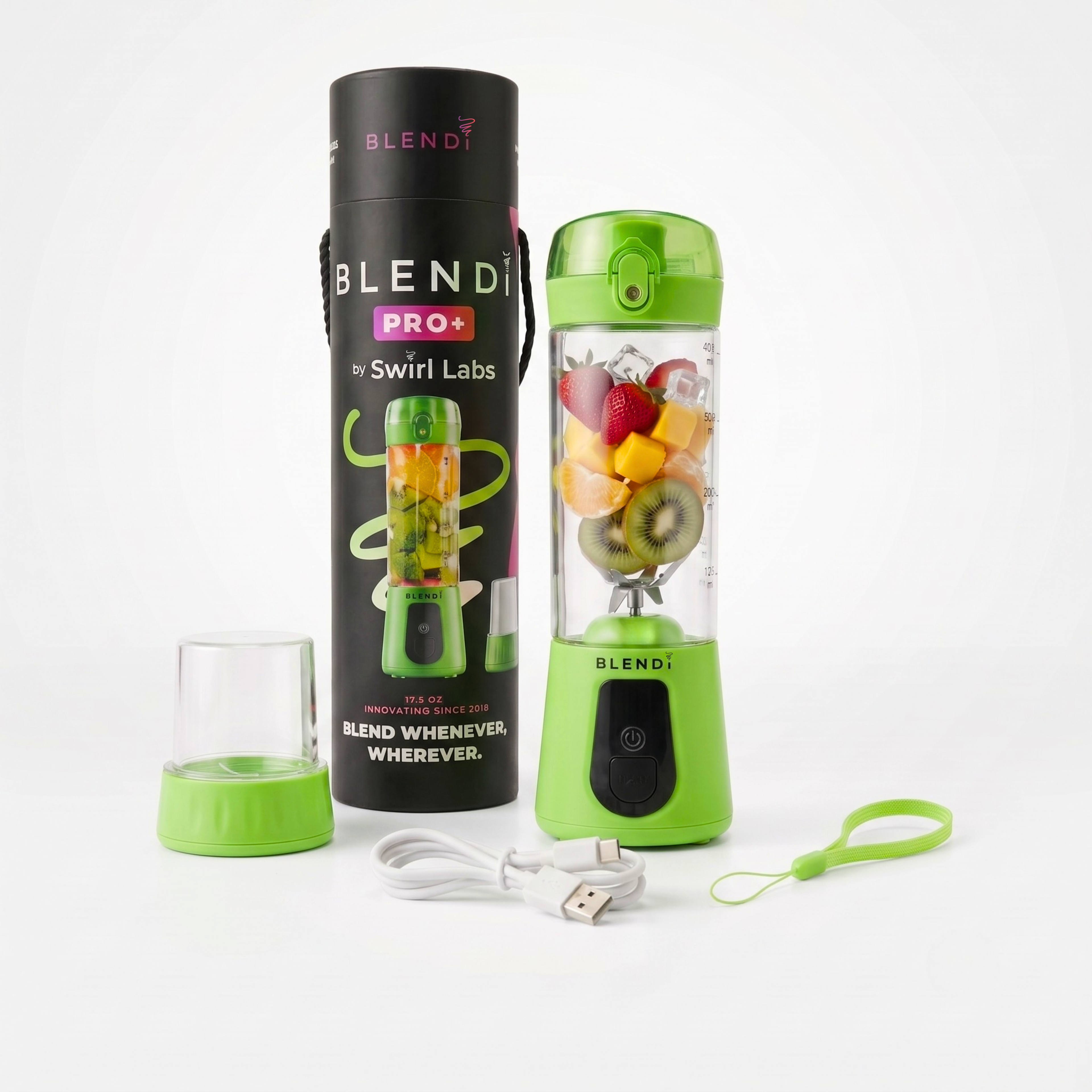 A portable blender bottle with a bright green base and lid, shown with its black cylindrical packaging tube, a small clear travel cup, a white USB charging cable, and a green wrist strap on a clean white background. The bottle is filled with fruit pieces.