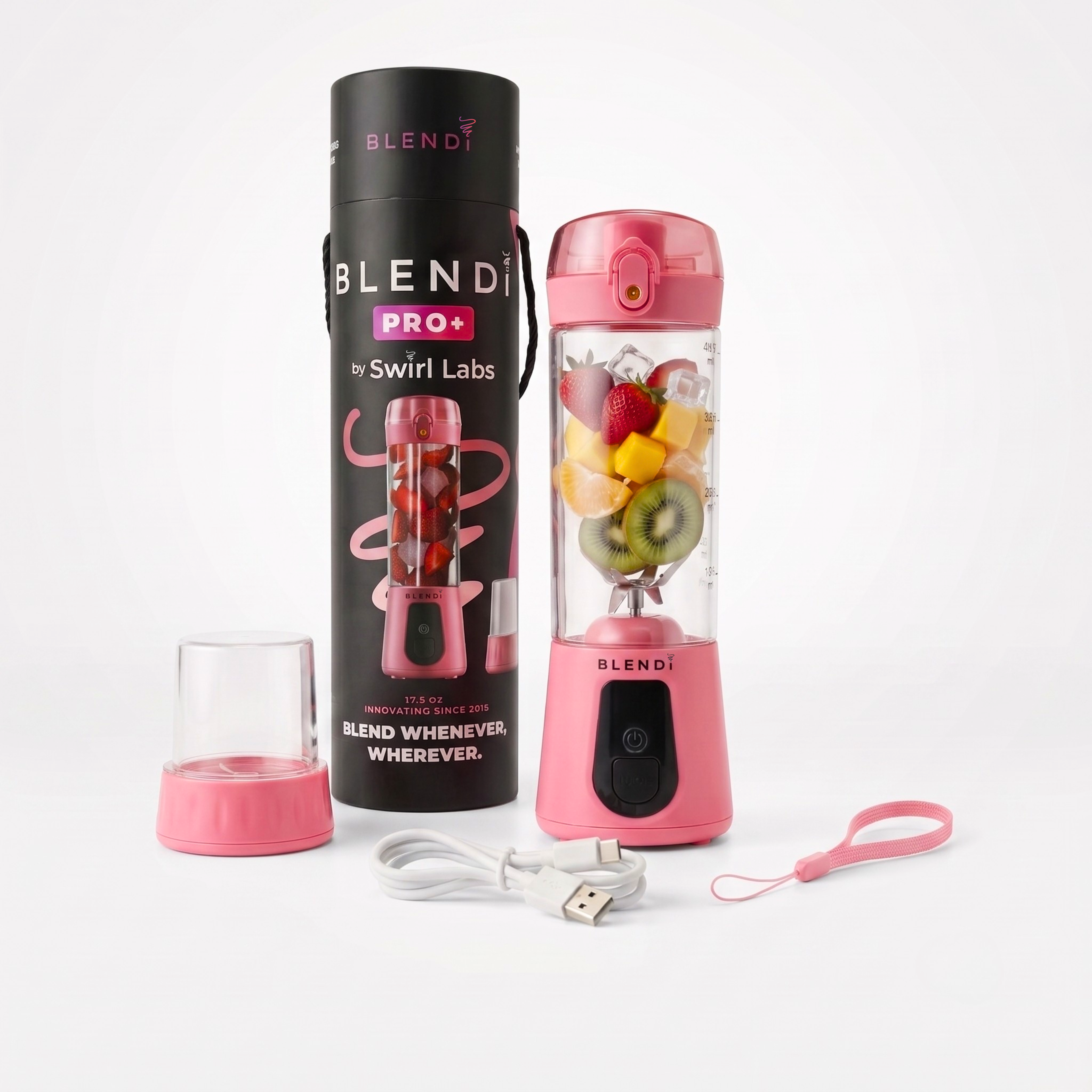 Pink Blendi Pro+ portable blender by Swirl Labs shown with its black cylindrical packaging, a small clear glass cup, USB charging cable, and carrying strap on a clean white background. The blender bottle is filled with fruit and is shown next to the packaging.