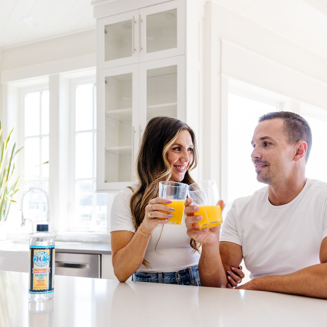 Man and woman in a kitchen holding glasses of orange juice with a bottle of K-Lime in the foreground.