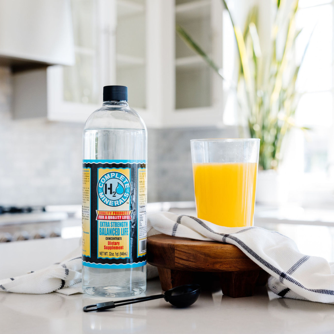 Bottle of Complete Health water on a kitchen counter with a glass of orange juice.