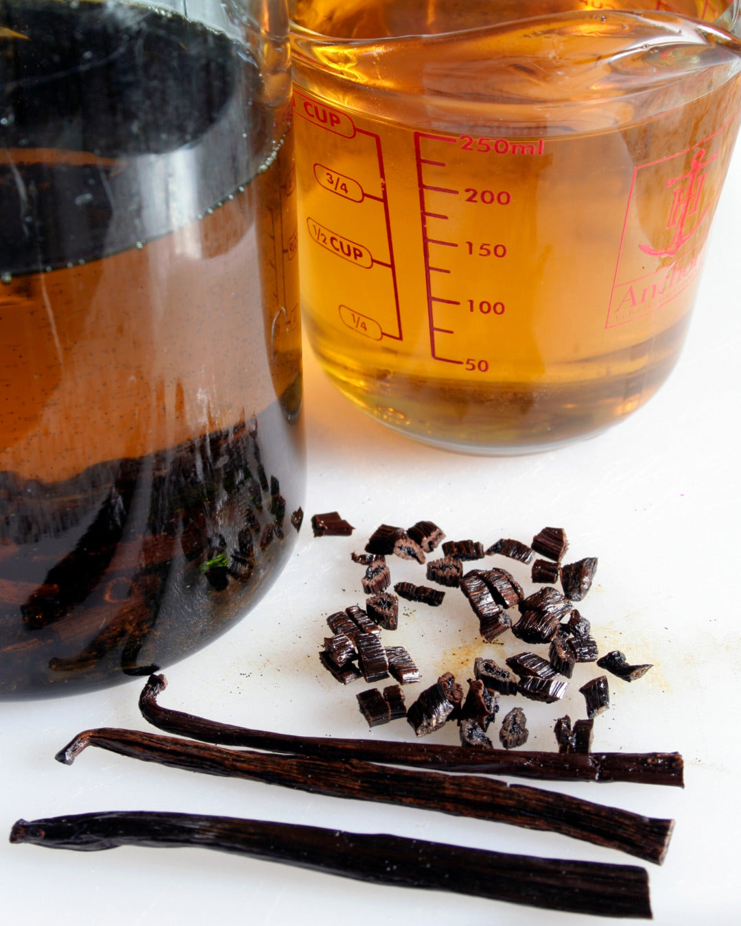 Vanilla beans, a glass of liquid, and vanilla extract on a white surface