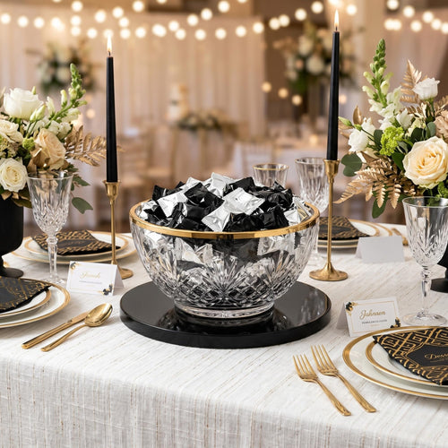 Black and silver individually wrapped butter mints displayed in a crystal serving bowl with gold trim on an elegant black, white, and gold party table, perfect for weddings, New Year's Eve, graduations, anniversaries, casino nights, and candy buffets.