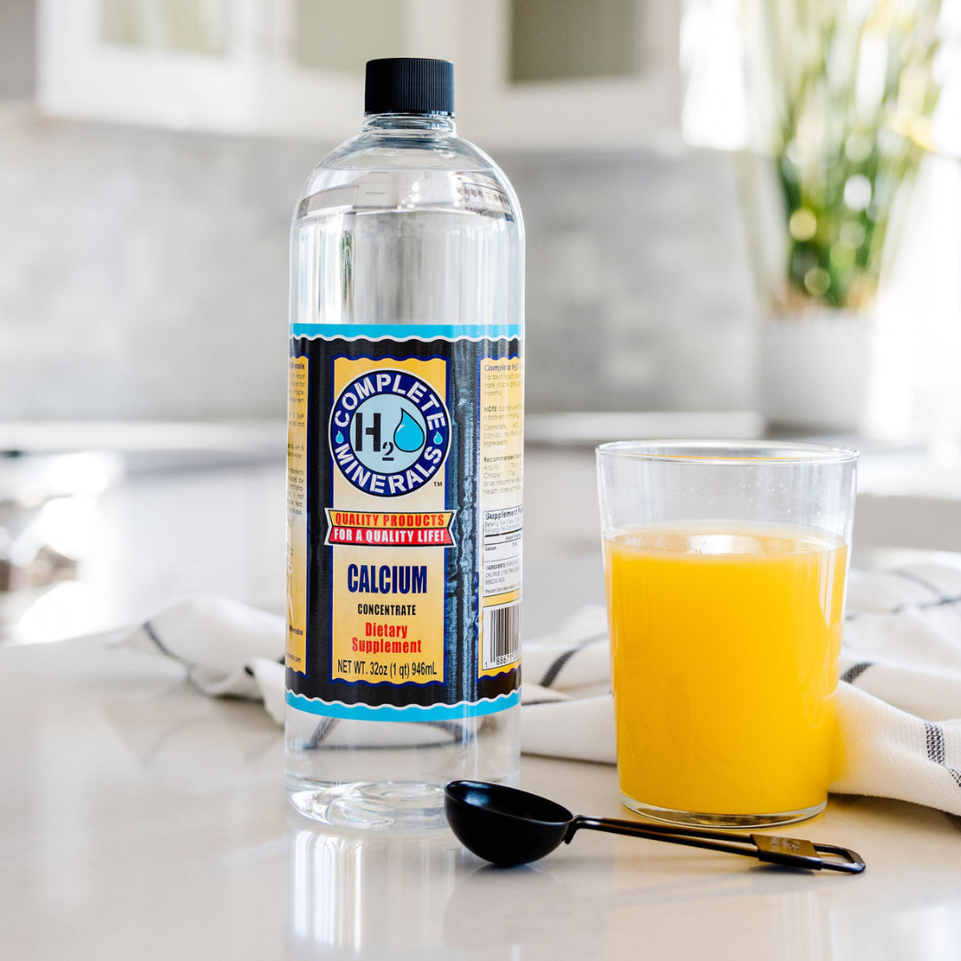 Bottle of 'Complete Minerals' supplement next to a glass of orange juice on a kitchen counter.