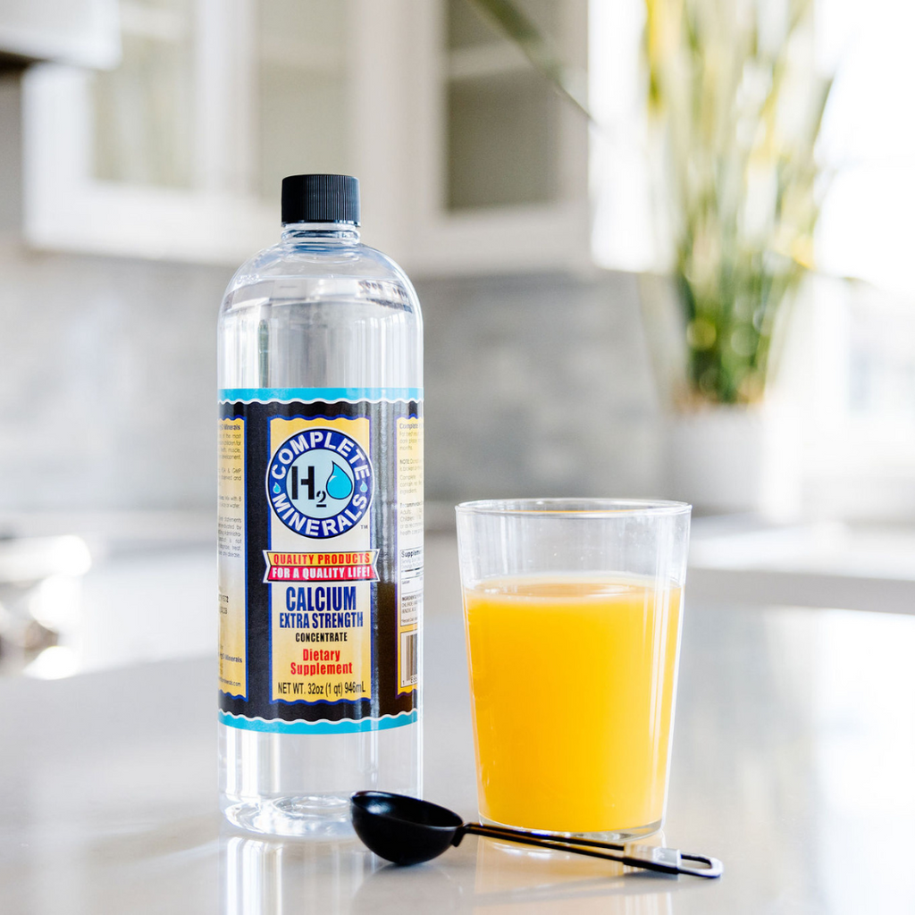 Bottle of Complete Mineral H2O with a glass of orange juice on a kitchen counter.