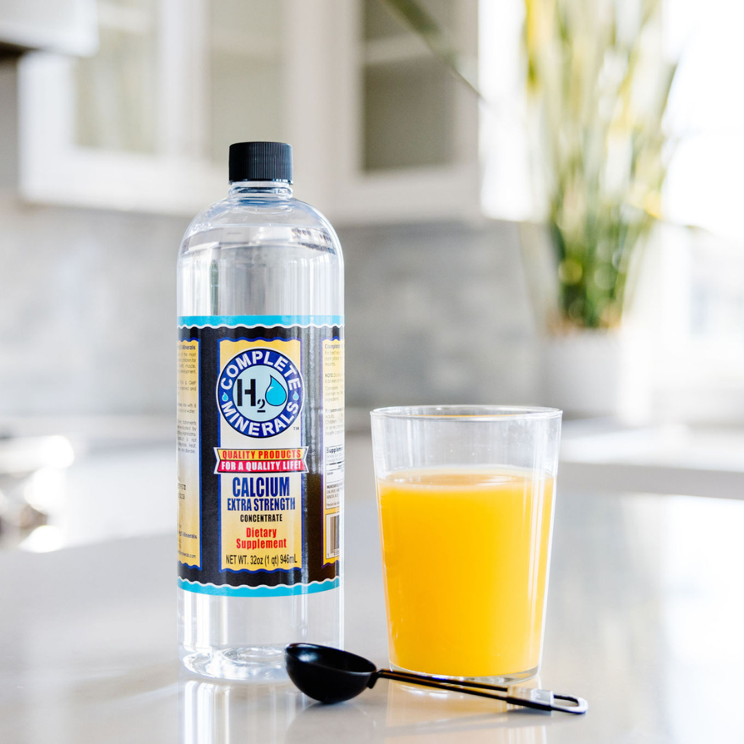 Bottle of Complete Mineral H2O with a glass of orange juice on a kitchen counter.