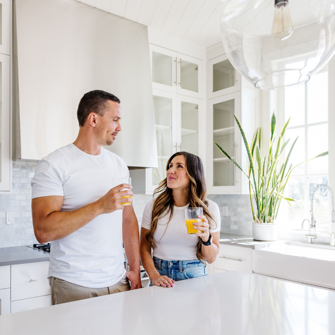 Man and woman standing in a modern kitchen, holding drinks.