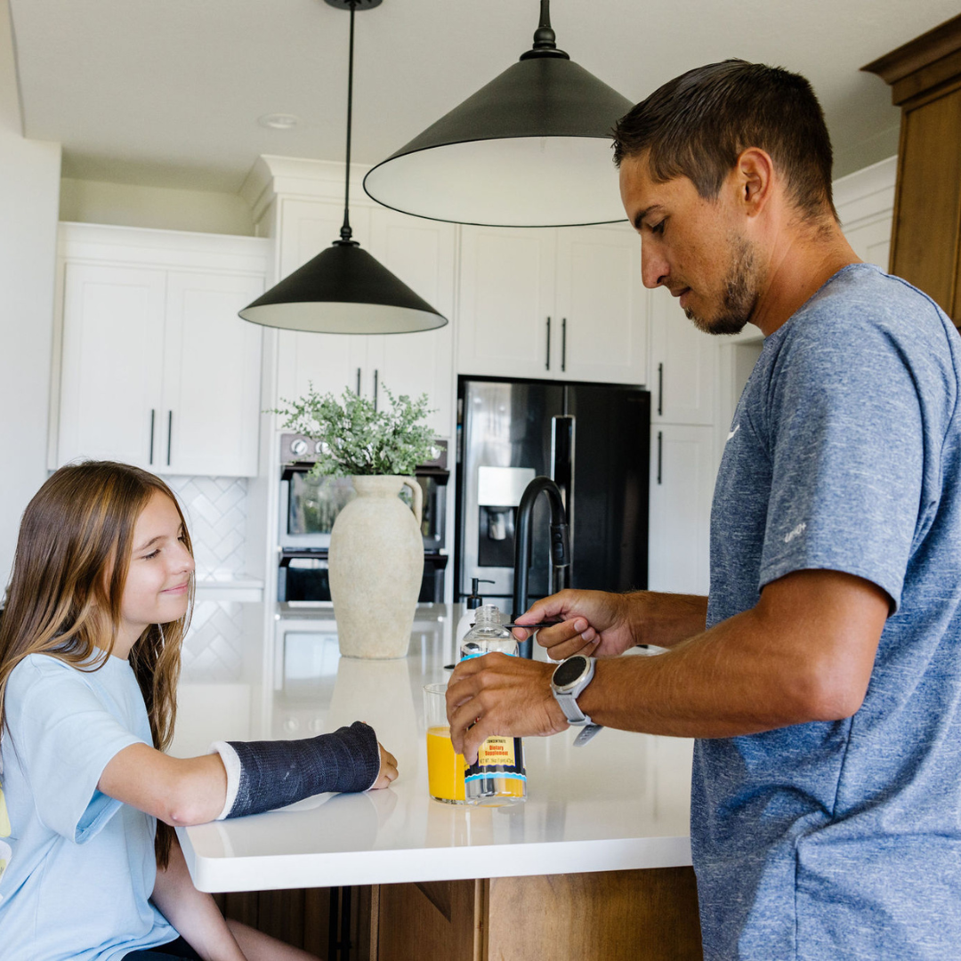 Man and young girl in a kitchen with a bottle of vitamins on the counter.