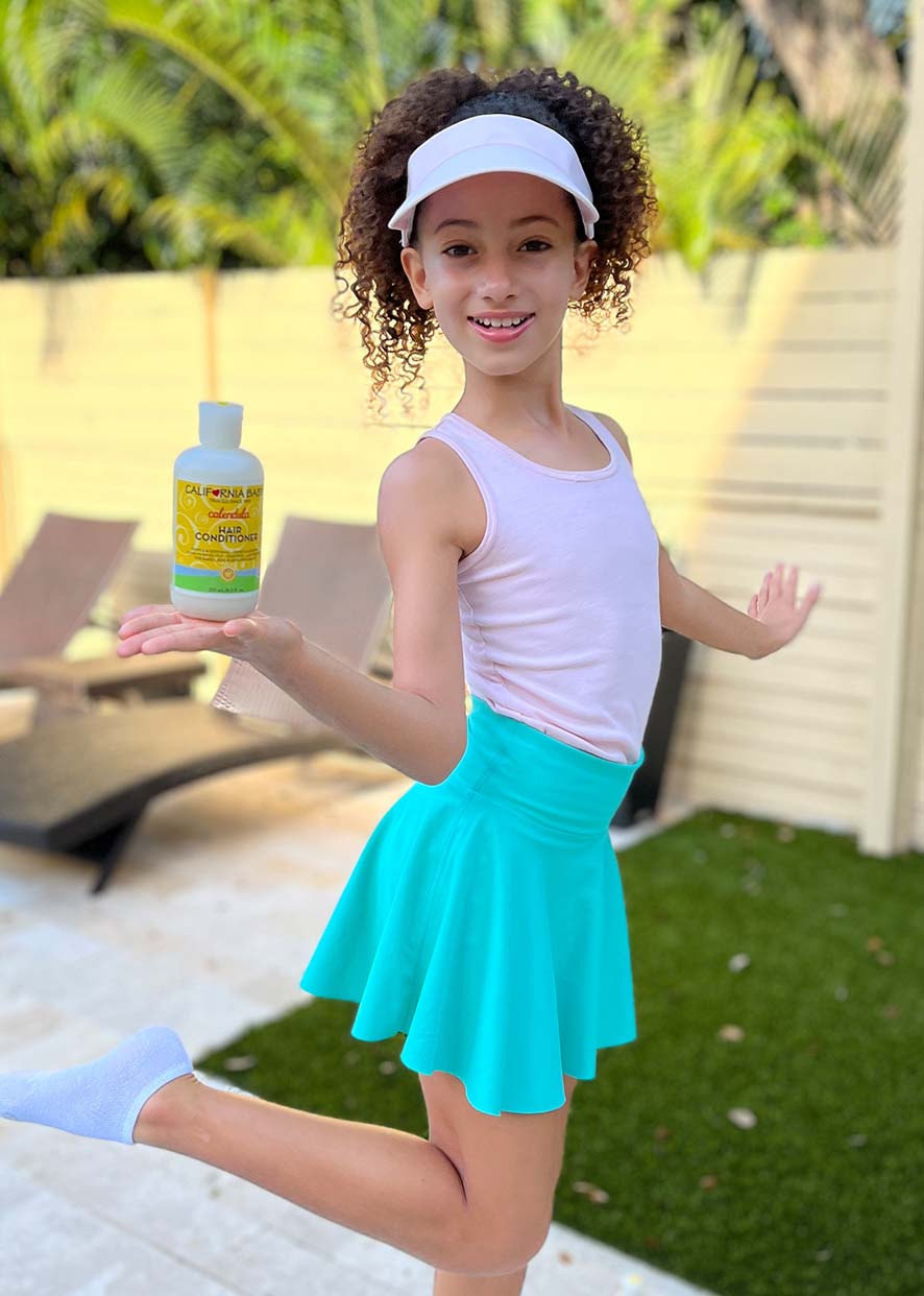 Young girl holding a bottle of sunscreen in a backyard setting. Calendula™ Hair Conditioner | Gentle Moisturizing Conditioner for Dry & Sensitive Hair (100% plant based ingredients, excludes water) certified organic
