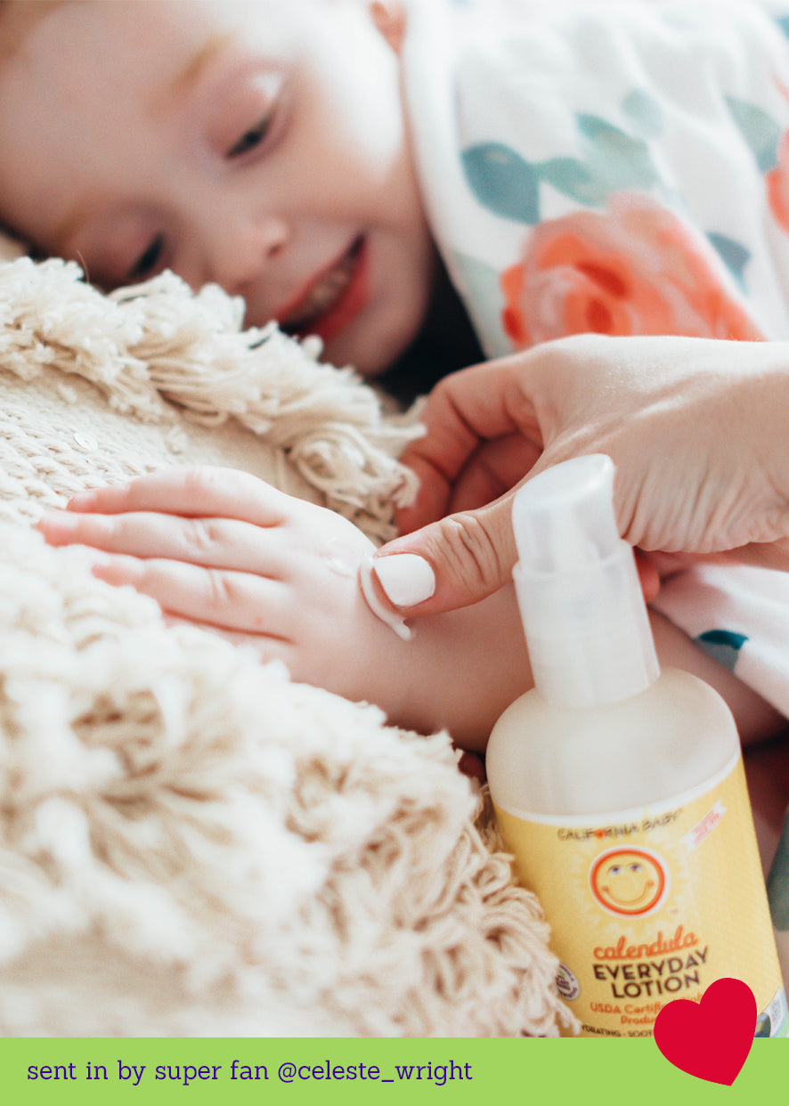 Child lying on a fluffy blanket with a bottle of Cuddledude Everyday Lotion held by an adult hand. California Baby Calendula™ Everyday Lotion for Sensitive Skin – Plant-Based Moisturizer with French Lavender | 8.5oz, 19oz, 64oz & 2oz
