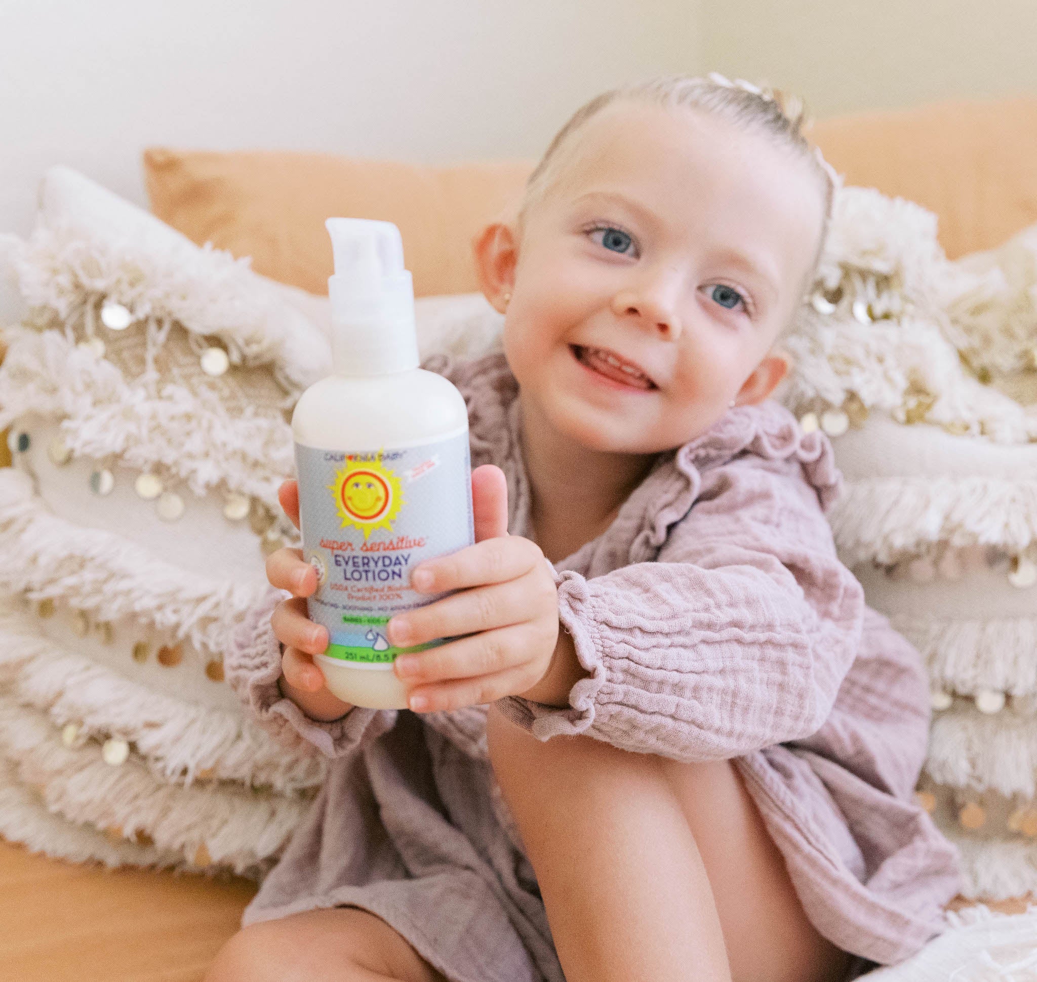 Child holding a bottle of Everyday Lotion with a white background California Baby® (No Fragrance) Super Sensitive™ Everyday Lotion