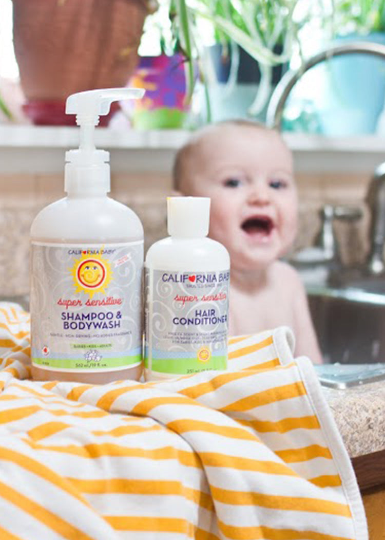 Two bottles of California Baby shampoo and conditioner on a towel with a baby in the background. California Baby® (No Fragrance) Super Sensitive™ Hair Conditioner - USDA Certified Biobased Product 100% Plant-Based
