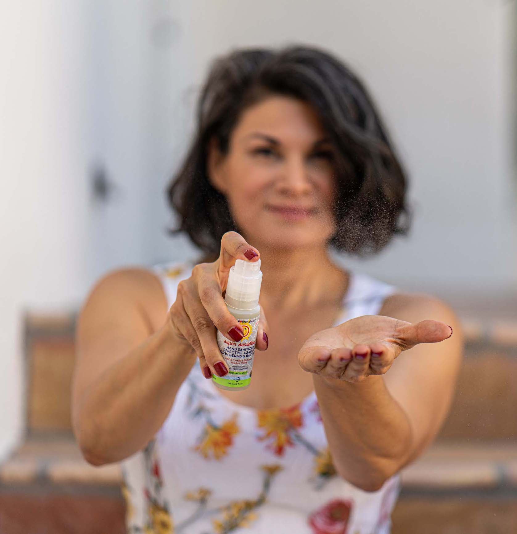 Woman demonstrating a bottle of powder with a blurred background. California Baby Super Sensitive Bath Essentials Bundle | Fragrance-Free Baby Shampoo, Body Wash, Conditioner, Calendula Cream, Lotion & Hand Sanitizer