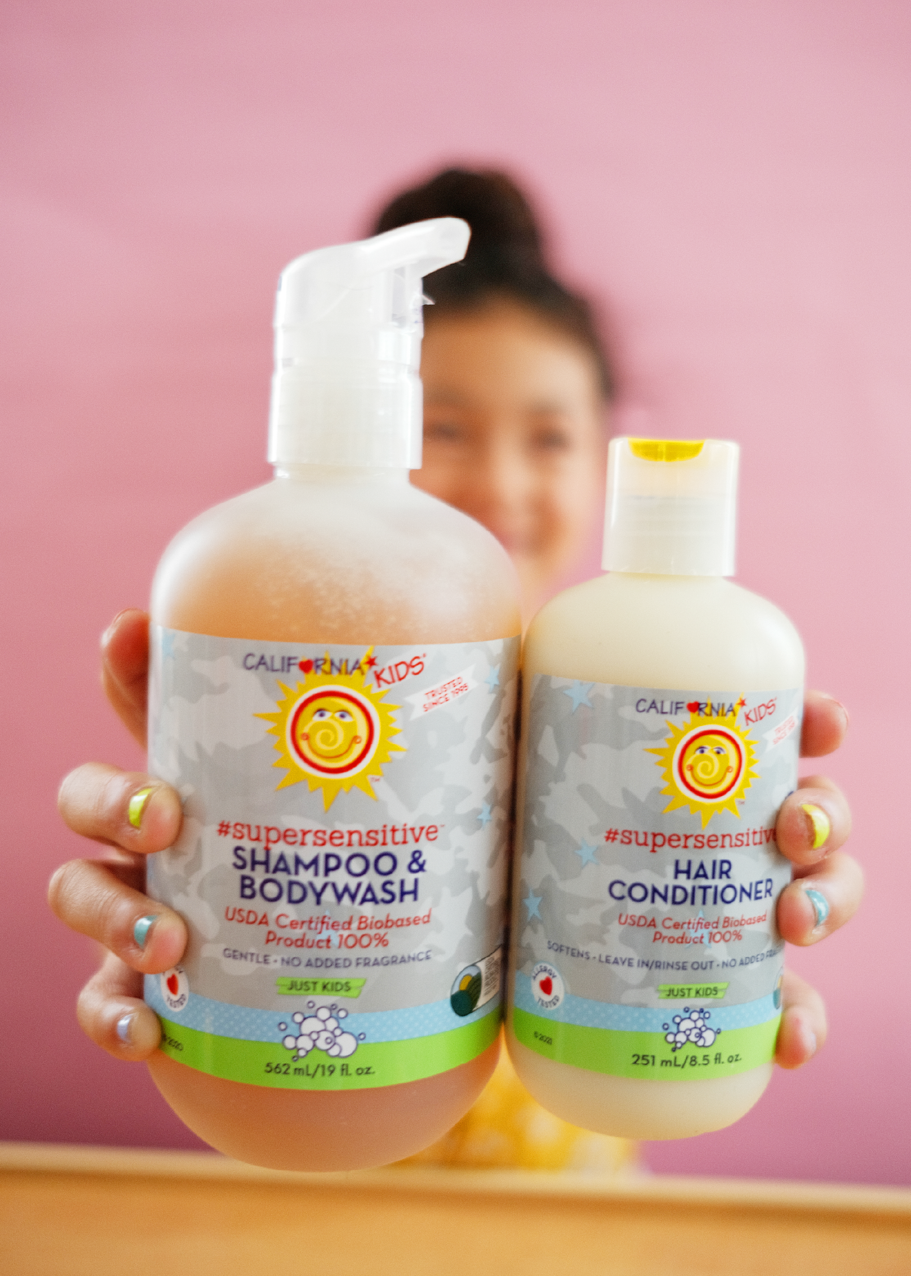 Two bottles of California Kids supersensitive shampoo and bodywash, and hair conditioner, held against a pink background. California Kids® Super Sensitive Essentials Set for Kids & Teens | Gentle Fragrance-Free Skin & Hair Care Gift Set