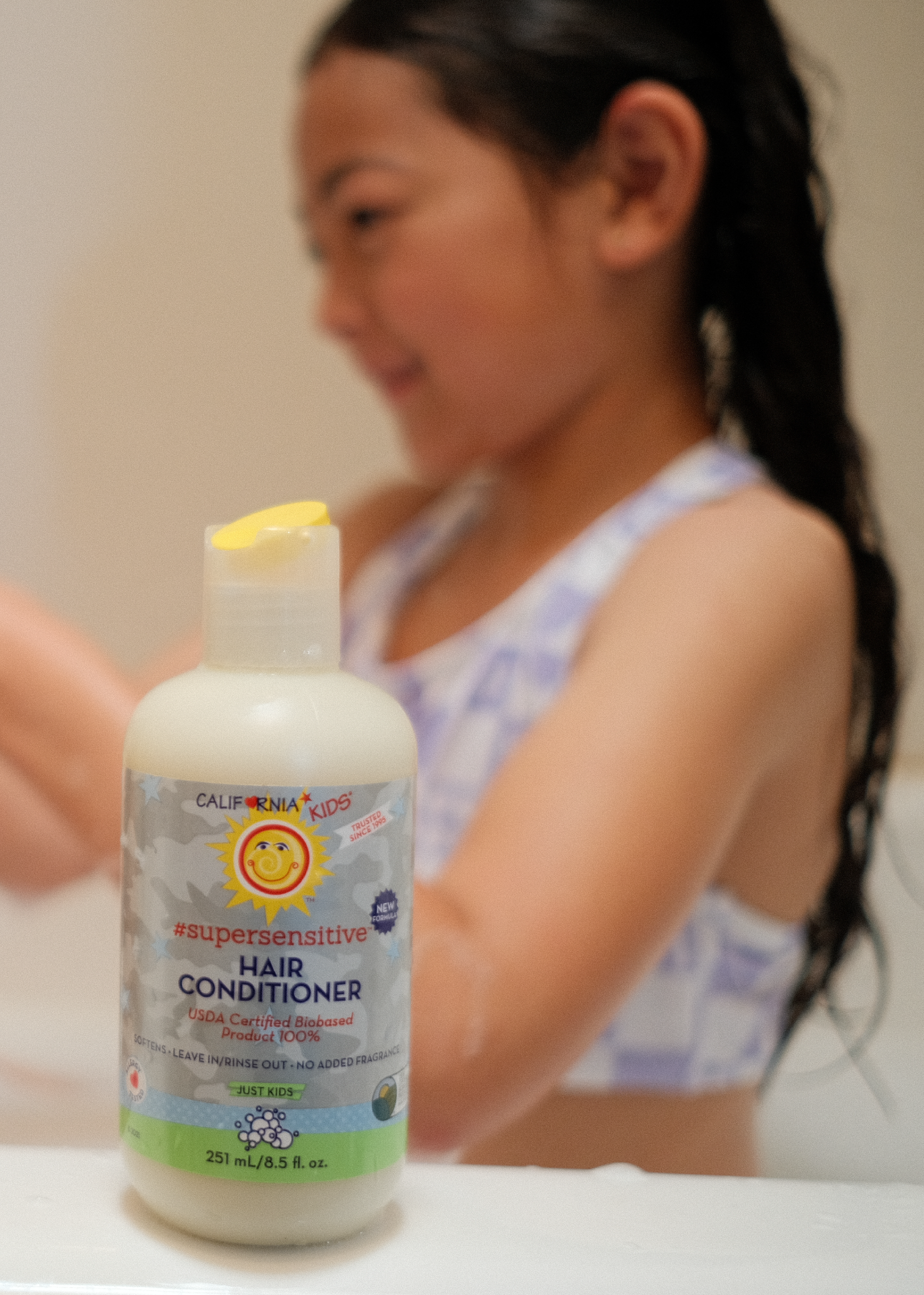 Bottle of California Kids hair conditioner with a blurred child in the background California Kids® Super Sensitive Essentials Set for Kids & Teens | Gentle Fragrance-Free Skin & Hair Care Gift Set