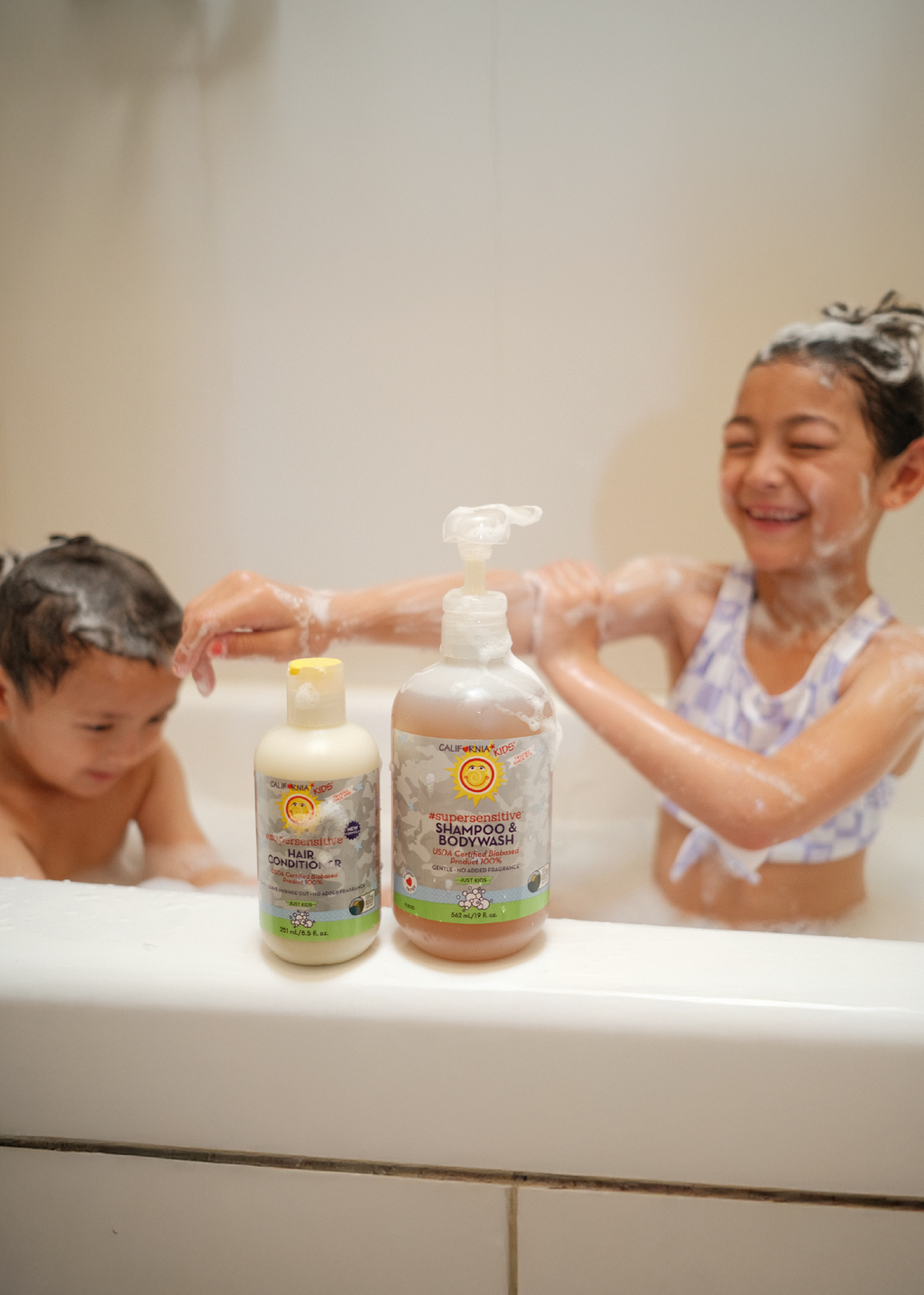 Two children in a bathtub with bottles of shampoo and body wash on the edge. California Kids® Super Sensitive Essentials Set for Kids & Teens | Gentle Fragrance-Free Skin & Hair Care Gift Set