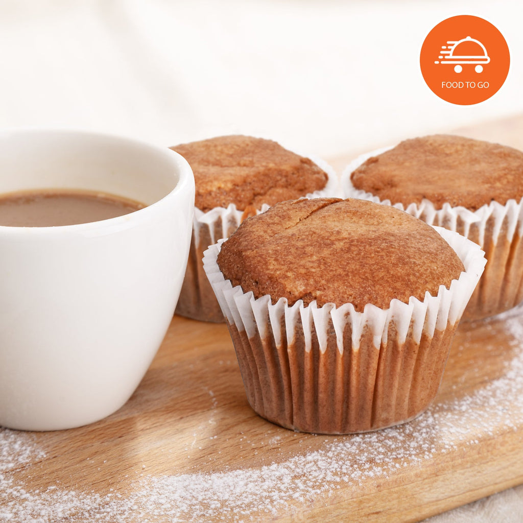Freshly baked cappuccino muffins in white paper liners arranged on a wooden board beside a steaming cup of coffee, lightly dusted with powdered sweetener, featuring a "Food To Go" badge. Ideal for keto, low-carb, sugar-free breakfast, snack, or grab-and-go bakery options.